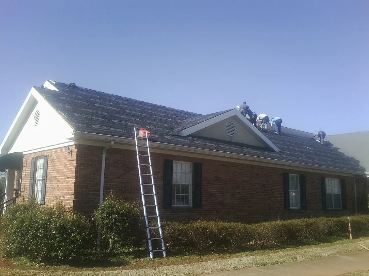 Crew tearing shingles off a brick ranch roof with a ladder set — Emergency Roof Repair work by our crew in Finley