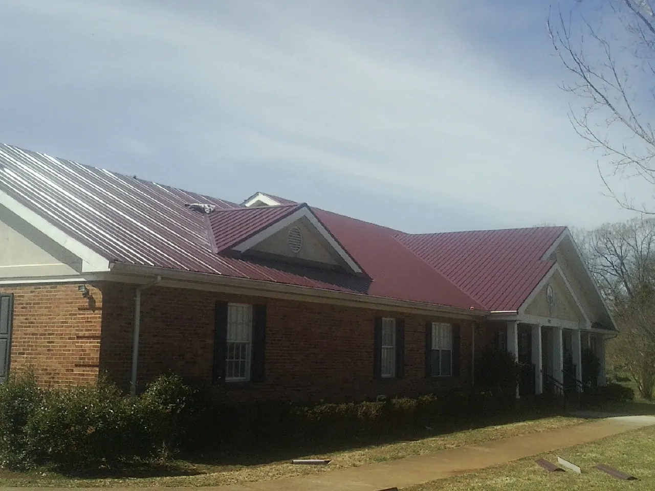 Red metal roof with gabled entries on a long brick building, from a Hail Damage Roof Repair job in Finley