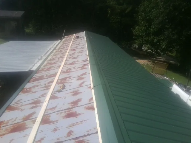Old rusted panels beside newly installed green metal roofing — Wind Damage Roof Repair by Roofing Brothers in Finley